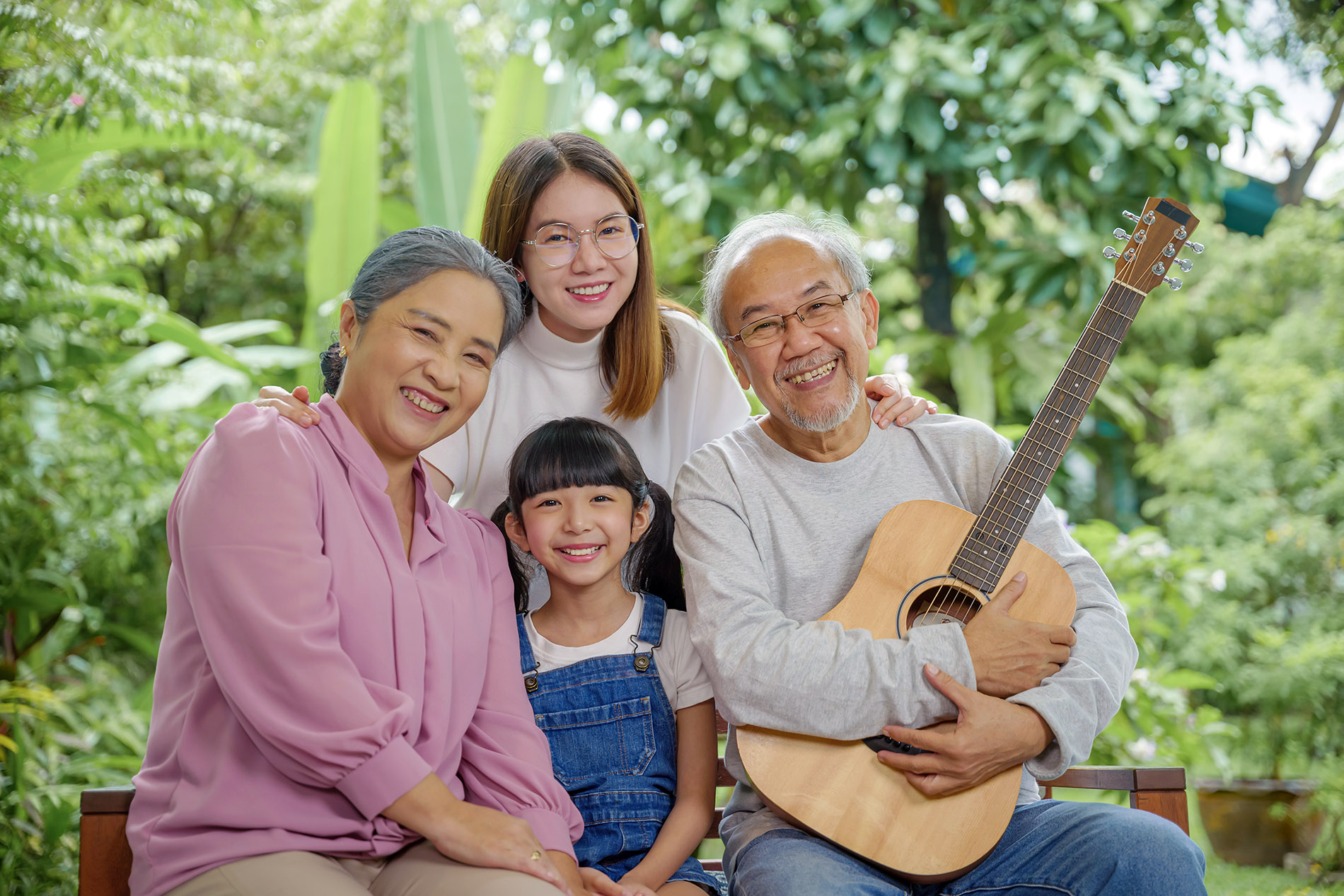 Asian senior elderly man or grandfather playing guitar while his grandmother and granddaughter singing song together